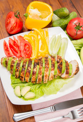 Chicken fillet with avocado and some vegetable on the side (tomato, cucumber, bell pepper) on a wooden background