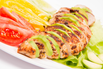 Chicken fillet with avocado and some vegetable on the side (tomato, cucumber, bell pepper) on a white background