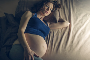 Pregnant woman feeling pain in her belly lying in bed with insomnia at night. Concept of pregnancy and health - obrazy, fototapety, plakaty