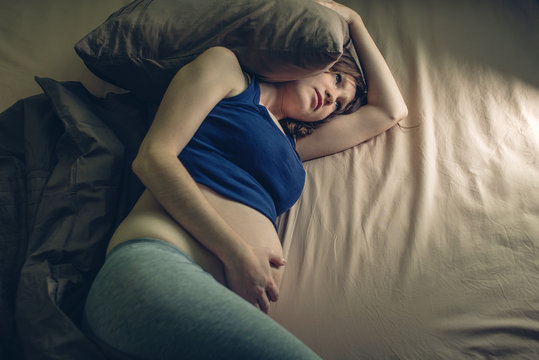 Pregnant woman feeling pain in her belly lying in bed with insomnia at night. Concept of pregnancy and health