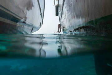 In the sea there are two yachts and from the side are visible the legs of a man. View half under water