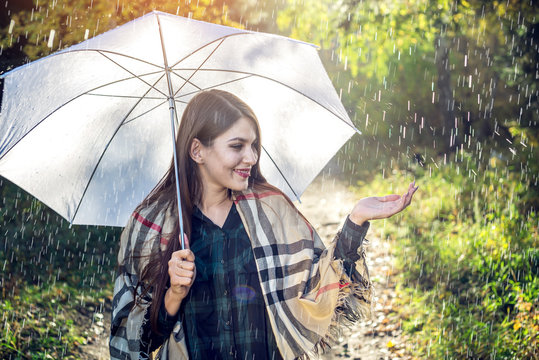 Happy young woman walking in a Sunny Park with a white umbrella in the rain. Concept of seasons and autumn mood