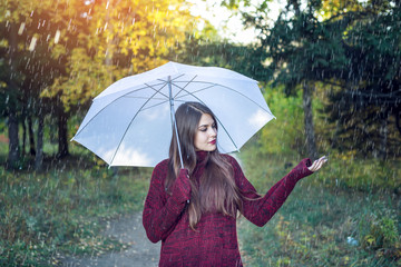 Happy young woman walking in a Sunny Park with a white umbrella in the rain. Concept of seasons and...