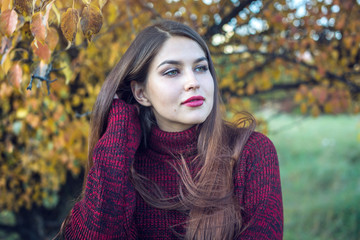 Beautiful colorful portrait of a woman in a red sweater and bright lipstick in the autumn Park. Concept of Autumn mood