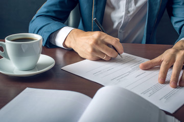 Businessman signs important legal documents on the desktop with Cup of coffee