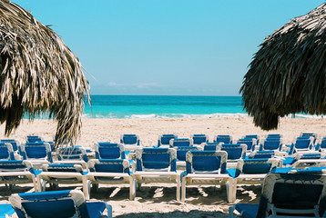 Two Palapas / Umbrellas flanking rows of empty beach chairs on a Caribbean beach