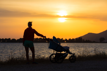 Fototapeta na wymiar Silhouette of mother with stroller enjoying motherhood at sunset landscape