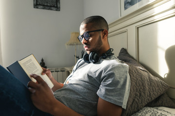 Latin man reading a book in bed.