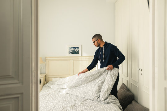 Latin man making bed at home.