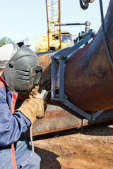 welder in coveralls makes a weld on a pipe of large diameter