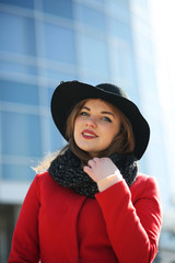 Cute businesswoman in a red coat against a background of glass