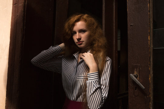 Sad red haired model with long lush hair. Woman posing in a old passage