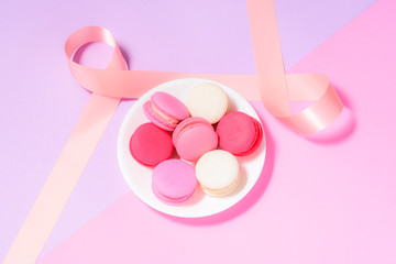Homemade Colorful macaroons or macaron on White plate with copyspace on pink and purple background