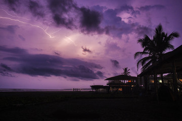A purple sky lights up with lightning on a tropical Mexican beach