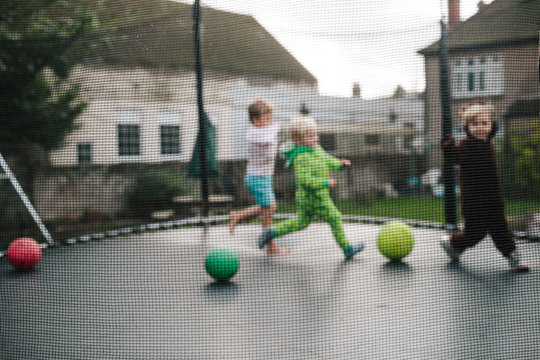 Three children are seen out of focus as the run around a trampoline.