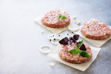 Raw hamburgers - cutlets from organic beef meat with spices and basil on a stone or slate background, top view with copy space.