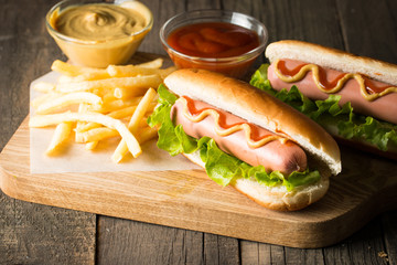 Tasty barbecue grilled hot dog with salad,yellow mustard, onion, ketchup, and French fries on wooden background. Junk and fast food concept.