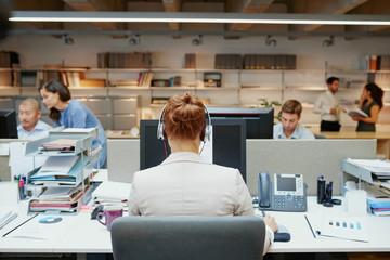 Back of business woman using headset facing coworkers rear view