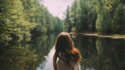 girl stands with his back to the camera. against the background of a beautiful river. green forest