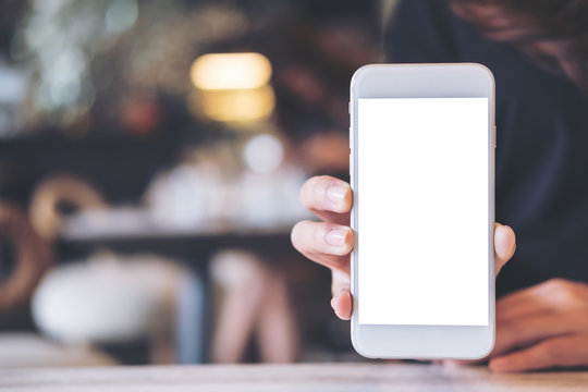 Mockup image of a woman holding and showing white mobile phone with blank screen on the table in modern cafe