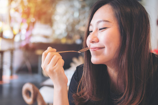 Closeup image of a beautiful Asian woman holding a spoon while enjoy eating food in modern cafe