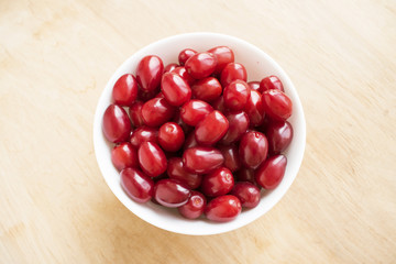  Cornelian cherry dogwood edible fruit.  Fresh  Dogwood (Cornus sanguinea) berries in round white bowl on wooden background. Benefits of Dogwood Berries