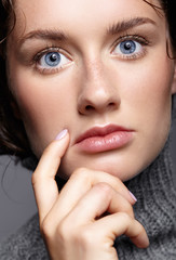 Beauty portrait of young woman in gray wool sweater. Brunette girl with bright blue eyes and day female makeup