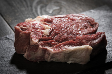 rohes Stück Rindfleisch auf Schieferplatte vor dunklem Hintergrund mit Gegenlicht