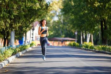 Young smiling sporty woman running on the road in the morning. Fitness girl jogging in park