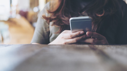 Closeup image of a woman's hands holding and using at smart phone on wooden table in vintage cafe