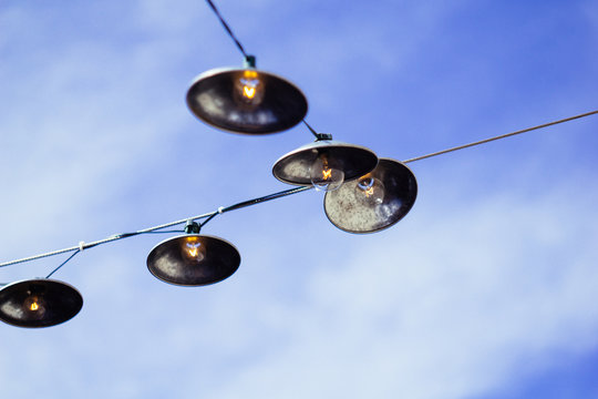 Patio lights against a blue sky with some hazy clouds.