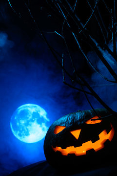 Scary Halloween pumpkin with glowing face on the background of the full moon in the fog