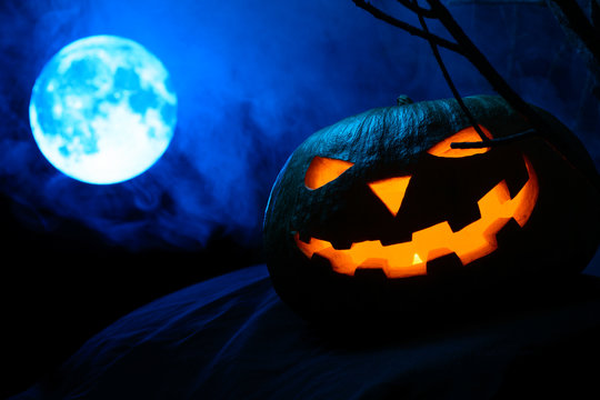 Scary Halloween pumpkin with glowing face on the background of the full moon in the fog