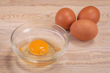 Egg with cracked eggshell on rustic wood table, yolk closeup