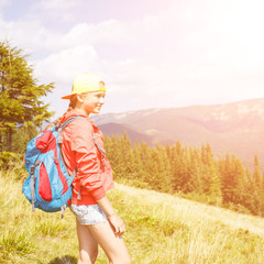 Young smiling teenage girl with backpack enjoying view in mountains. Summer vacation hiking concept background with copy space