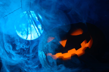 Fototapeta premium Scary Halloween pumpkin with glowing face on the background of the full moon in the fog