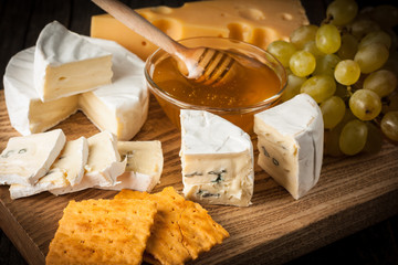 Slate board with various cheese and a glass of red rose wine. Brie. Camembert. Gouda, Masdaam, Roquefort, Cheddar and grapes on a wood with nuts, honey, crackers, blue cheese. Italian, French cheese.