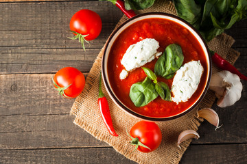 Chili tomato soup with sour cream sauce, cottage cheese, basil and red hot peppers on wooden background. Healthy, vegan and dieting lunch and dinner concept.