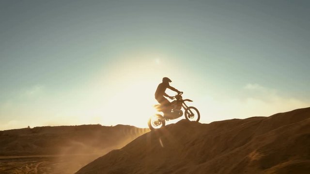 Side View Footage of the Professional Motocross Motorcycle Rider Driving on the Dune and Further Down the Off-Road Track. It's Sunset and Track is Covered with Smoke/ Mist. 4K UHD.