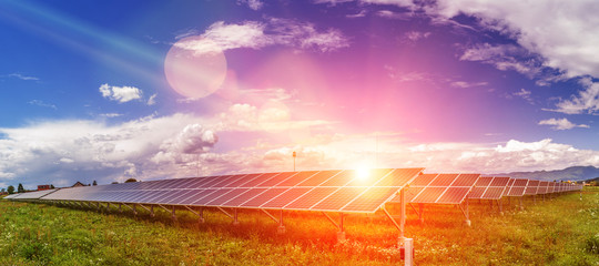 Panels of the solar energy plant under the blue sky with white clouds with sun flare hitting the...