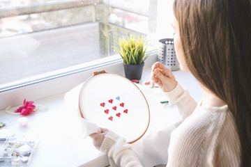 Young woman embroidering small red hearts
