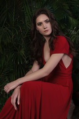 Obraz na płótnie Canvas brunette girl in red dress sitting among tropical leaves
