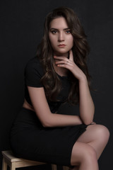 Naklejka premium portrait of a beautiful girl in black clothes sitting dark background