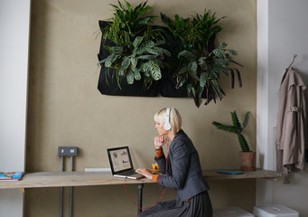 Young attractive sophisticated blonde woman in cafe working on laptop listening to music headphones enjoying hot fresh coffee