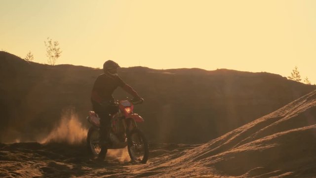 Side View Shot Professional Motocross Motorcycle Rider Drives on the Dune and Stops. It's Sunset and Track is Covered with Smoke/ Mist. Shot on RED EPIC-W 8K Helium Cinema Camera.