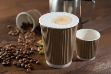 Latte and espresso in paper cups on a wooden background with scattered coffee beans