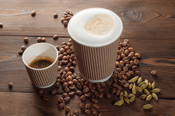 Latte and espresso in paper cups on a wooden background with scattered coffee beans