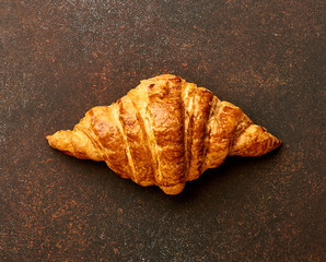 Croissant on brown concrete background. Bakery product. Top view.