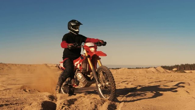 Professional FMX Motorcycle Rider Twists Full Throttle Handle and Starts Riding on the Sandy Off-Road Track. Scenic Sunset. Shot on RED EPIC-W 8K Helium Cinema Camera.