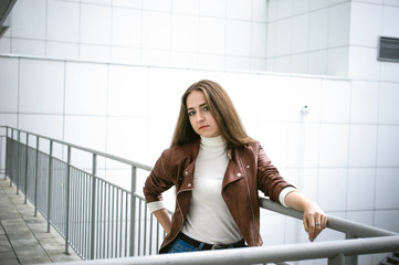Fototapeta premium street portrait of a female student in fashionable clothes, blue jeans and a brown jacket, outdoors